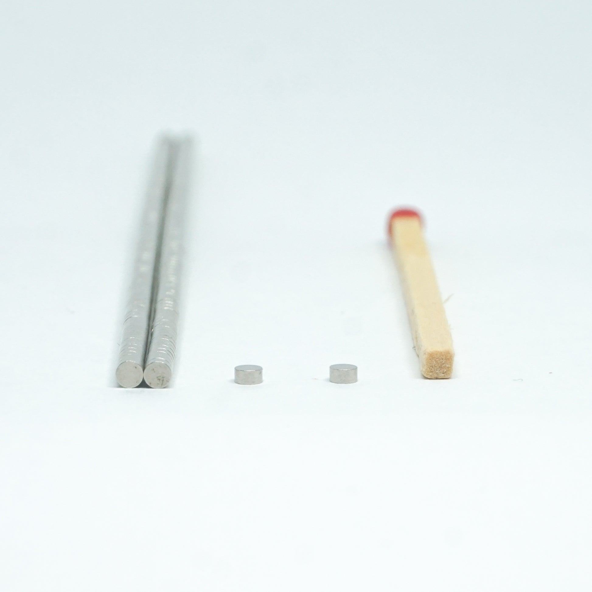 The image shows two cylindrical magnets alongside a matchstick for scale.